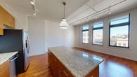 This well-appointed two-bedroom, two-bathroom residence in downtown Detroit offers a thoughtfully designed single-floor layout. The open-concept living and kitchen area is a standout feature, centered around a generous granite-topped island illuminated by a pendant light and complemented by track lighting overhead. Warm hardwood floors flow throughout, adding richness and continuity to the space. The kitchen is fully equipped with stainless steel appliances, including a refrigerator with ice maker, range, and built-in microwave, alongside abundant warm-toned wood cabinetry and granite countertops. Large windows in the living area frame views of Detroit's urban streetscape, filling the space with natural light. Both bedrooms are well-proportioned with clean white walls, hardwood flooring, and ample room for furnishings. The two bathrooms are finished with consistent design elements: warm wood vanities, granite countertops, and neutral tile work. One bathroom features a glass-enclosed walk-in shower with a built-in bench, while the second includes a soaking tub with a glass sliding door. The overall aesthetic is clean, modern, and urban, making this a practical and attractive residence in the heart of Detroit.
