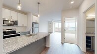 Located at 118 N Prince St in the heart of Lancaster, PA, this thoughtfully designed one-bedroom, one-bathroom residence offers a clean, modern aesthetic throughout. The open-concept kitchen and living area serves as the centerpiece of the unit, featuring a granite-topped peninsula with pendant lighting, white shaker cabinetry, gray lower cabinets, and a full suite of stainless steel appliances including a range, microwave, and refrigerator. Light wood-look flooring ties the space together with a bright, contemporary feel. The bedroom is a comfortable retreat with plush carpeting, a ceiling fan, and large sliding glass doors that open to a private balcony overlooking the Lancaster cityscape. A generous walk-in closet with built-in wire shelving provides ample storage. The bathroom continues the modern design language with a granite-topped vanity, gray cabinetry, and wood-look tile flooring. A dedicated laundry room houses a stacked full-size washer and dryer alongside open shelving for added convenience. Crisp white walls and abundant natural light from multiple windows create an airy, welcoming ambiance throughout this well-appointed urban residence.