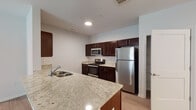 Located at 7487–7499 Outer Loop in Louisville, Kentucky, this single-floor residence offers a clean, contemporary design with consistent finishes across every room. The kitchen serves as a functional centerpiece, featuring rich dark-wood shaker cabinetry, light granite countertops, a white subway tile backsplash, and a full suite of stainless steel appliances including a refrigerator, electric range, and built-in microwave. A peninsula with a double-basin sink extends the counter space and connects the kitchen to the open living area, which is finished with smooth light-toned luxury vinyl plank flooring found throughout the entire unit. The living space is bright and open, with recessed lighting and clearly defined areas for relaxing and dining. Multiple bedrooms offer natural light through horizontal-slatted windows, with ceiling fans providing additional comfort in the larger rooms. The primary bathroom is well-appointed with a glass-enclosed tiled shower, granite-topped dark wood vanity, and large mirror, while a second bathroom includes a full soaking tub with a showerhead combo and matching vanity finishes. The neutral color palette and modern hardware selections create a cohesive, move-in-ready atmosphere throughout the entire space.