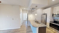 This 520 square foot apartment in Charlotte, NC, offers a well-designed living space with a modern aesthetic. The single-floor layout comprises one bedroom, one bathroom, a kitchen, and a closet, making efficient use of the available area. The kitchen is a standout feature, boasting sleek white cabinetry, stainless steel appliances, and a striking granite countertop with a double sink. An island with a matching granite top provides additional prep space and casual dining options. Pendant lighting adds a touch of elegance to the kitchen area. The bedroom, measuring 160 square feet, features a ceiling fan and ample natural light from a large window. Throughout the apartment, wood-look flooring creates a warm, cohesive feel. The bathroom is equipped with a walk-in shower, granite-topped vanity, and modern fixtures. Climate control is ensured with both central air conditioning and a wall-mounted unit. The overall design emphasizes clean lines, neutral colors, and contemporary finishes, creating a fresh and inviting living environment.