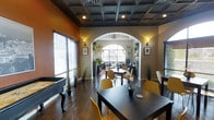 This single-story community space is thoughtfully designed to offer residents a variety of social and functional amenities. The interior lounge is a standout area, showcasing a coffered ceiling with recessed lighting and a warm, earthy color palette of deep orange and neutral tones. Dark hardwood floors anchor the space, while mustard-yellow chairs and dark dining tables create a modern, inviting atmosphere. A graceful arched doorway connects the main seating area to a secondary lounge space, where lush hanging and potted greenery adds a refreshing, natural element. Large windows fitted with blinds allow natural light to fill the room. Wall sconces provide warm accent lighting throughout.

A covered mailroom corridor features white shiplap-style walls, large-format tile flooring, and a full bank of individual mailboxes. A beverage station adds a welcoming touch for residents passing through.

Outdoors, the resort-style pool area is a focal point of the community. Surrounded by a spacious patio, it features an array of lounge chairs, umbrella-shaded bistro tables, and elegant white canopy cabanas. Mature trees and distant hills frame the backdrop, creating a serene, upscale outdoor retreat.