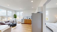 Unit 502 at 49 Long St in Jersey City offers a thoughtfully designed one-bedroom, one-bathroom layout that maximizes every square foot of its compact footprint. The open-plan living and kitchen area is anchored by warm light wood flooring that flows throughout, creating a cohesive and inviting atmosphere. Large windows flood the space with natural light while framing elevated views of the Jersey City skyline and the waterway beyond, giving the unit a distinctly airy feel despite its efficient size.

The kitchen is outfitted with a clean two-tone design, pairing white upper cabinetry with natural wood lower cabinets and a white quartz countertop. Stainless steel appliances — including a gas range, microwave, dishwasher, and refrigerator — complete the functional setup. A black matte faucet adds a modern contrast to the bright, minimalist aesthetic.

The bedroom is a serene retreat, featuring a large window with open views, a closet with double doors, and continued light wood flooring. The room offers enough space for a full bedroom suite while maintaining a calm, uncluttered feel.

The bathroom is finished in marble-style tile from floor to ceiling, with a soaking tub and shower combination, a wood-toned vanity with a white basin, and a bold black-framed mirror with matte black fixtures — lending a sleek, contemporary character to the space.