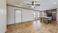 Located at 606 S Park St in Ogden, Kansas, this single-story, 3-bedroom, 2-bathroom home offers a practical and modern layout. The open-concept main living area is anchored by a well-appointed kitchen featuring rich dark wood cabinetry, granite-look countertops, a central island with a built-in sink, a wall-mounted range hood, and black appliances. Wood-look plank flooring runs throughout the main living and kitchen areas, complementing the warm, neutral color palette. Recessed lighting and a ceiling fan with light kit illuminate the combined kitchen and living space, which is brightened by multiple windows. The living area provides a welcoming entry with a paneled front door topped by a transom window. The three bedrooms offer plush carpeting and ample natural light, with the generously sized primary bedroom featuring an en-suite bathroom equipped with a double-sink vanity with granite countertops, a soaking tub, open shelving, and wood-look tile flooring. The secondary bathroom includes a standard tub and toilet. Additional spaces include hallways, a pantry, a closet, and an outdoor patio, rounding out the functional layout of this efficiently designed home.