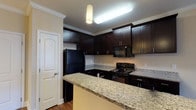 This single-floor, two-bedroom, two-bathroom unit offers a well-organized layout with distinct living and sleeping areas. The kitchen is a standout feature, showcasing rich dark espresso cabinetry with ample storage, granite countertops, and black appliances including a refrigerator, electric range, and built-in microwave. Pendant lighting and a peninsula with a breakfast bar add both functionality and visual interest. Crown molding and hardwood-style flooring enhance the kitchen and living areas, contributing to a polished, cohesive aesthetic.

Both bedrooms are generously proportioned, finished with plush neutral carpeting and ceiling fans with light fixtures. Multiple windows dressed with horizontal blinds allow natural light to fill each room, offering views of the surrounding exterior. The bedrooms provide a comfortable, quiet retreat.

Each bathroom is well-appointed with dark vanity cabinetry, granite-topped counters, and tub-shower combinations with chrome fixtures. One bathroom features tile flooring and a window for natural light, while both maintain a clean, neutral palette. The unit also includes a private patio, extending the living space outdoors.