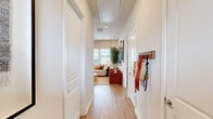 This single-story, 2-bedroom, 3-bathroom home offers a thoughtfully designed layout across a comfortable footprint. Light hardwood-style flooring flows throughout, complementing the neutral color palette that gives the space a clean, cohesive feel.

The entry hallway welcomes residents with practical wall hooks and leads directly into the heart of the home. The kitchen is a standout feature, boasting crisp white shaker cabinetry, stainless steel appliances, white countertops, a tile backsplash, pendant lighting over a central island with seating, and ample storage including tall upper cabinets. The adjacent living room is bright and open, fitted with a ceiling fan and large windows that invite natural light.

The primary bedroom is a serene retreat, featuring a ceiling fan, large windows with blinds and curtains, and direct access to a private en-suite bathroom. The en-suite includes a dual-sink white vanity with quartz countertops and a glass-enclosed walk-in shower with tile surround. The second bedroom is equally well-lit, offering generous space, a ceiling fan, and its own access to a bathroom.

Two hallways and two closets provide practical storage throughout. Outside, a private yard area features turf grass, a concrete patio, and a lush green hedge wall, creating an inviting and low-maintenance outdoor retreat.