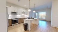Located in Chamblee, GA, this well-designed 2-bedroom, 2-bathroom residence offers a thoughtful layout across a single floor. The open-concept kitchen serves as the heart of the home, showcasing two-tone cabinetry that pairs crisp white upper cabinets with warm wood-grain lower cabinets, complemented by a geometric tile backsplash and sleek white quartz countertops. A central island with pendant lighting overhead provides additional prep and seating space, while stainless steel appliances — including a side-by-side refrigerator with ice maker, electric range, and over-the-range microwave — complete the modern aesthetic. Light wood-look flooring flows seamlessly through the kitchen and living areas, lending warmth and continuity. Large windows allow natural light to fill the space, with views to an outdoor balcony area. Both bedrooms are carpeted and offer a calm, neutral palette, with the primary bedroom featuring generous proportions and access to a dedicated walk-in closet outfitted with wire shelving. Two full bathrooms serve the residence; one includes a long vanity with a white countertop and framed mirror, while the second features a tub-shower combination with floor-to-ceiling tile surround. The overall design is clean, contemporary, and move-in ready.