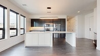 Located on North Road in Brecksville, Ohio, this single-floor space showcases a thoroughly modern design characterized by clean lines, neutral tones, and high-quality finishes throughout. Dark-framed windows invite abundant natural light and offer open views of the surrounding landscape, creating a bright and airy atmosphere across all rooms.

The kitchen serves as a focal point of the space, featuring a large white quartz island with an integrated sink and seating overhang, dark flat-panel cabinetry extending to the ceiling, stainless steel appliances including a French door refrigerator and built-in microwave, and a crisp subway tile backsplash. A statement oval pendant light anchors the space above the island. Dark hardwood-style flooring flows consistently through the main living areas, complementing the two-tone cabinetry.

The living area offers generous proportions with a clean white palette, while a compact built-in cabinet provides additional storage near the entry. Bedrooms are well-sized, with large black-framed windows providing outdoor views and abundant light. A dedicated walk-in closet includes built-in shelving and hanging rods for organized storage, and a paneled door with matte black hardware adds a refined touch.

The bathroom features large-format stone-look tile flooring, a dark floating vanity with gray quartz countertop, a backlit mirror, and a glass-enclosed shower, all unified by matte black fixtures.