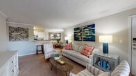 Located in Sandy Springs, Georgia, this well-designed three-bedroom, two-bathroom residence offers a comfortable and thoughtfully laid-out single-floor plan. The living room makes a welcoming impression with its textured ceiling, crown molding, plush carpeting, and an abundance of natural light streaming through large windows dressed with bold navy and cream drapes. Vibrant abstract artwork and warm accent lighting contribute to an inviting, curated ambiance.

The open layout connects the living area seamlessly to the dining space and kitchen. The dining area features warm hardwood flooring, wainscoting, a pendant light fixture, and a large framed mirror that adds depth and elegance. The galley-style kitchen is equipped with white cabinetry, dark granite countertops, stainless steel appliances, and hardwood floors, offering both functionality and style.

Each bedroom is generously sized with soft carpeting and large windows that bring in natural light. The primary bedroom provides a serene retreat with neutral tones and tasteful décor. The bathrooms include granite vanity surfaces and classic white tile. A dedicated in-unit laundry closet with full-size washer and dryer adds everyday convenience. This residence combines practical living with polished design details throughout.