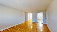 This single-floor space offers a clean, functional layout with a cohesive design throughout. Warm-toned hardwood floors extend across the living areas and bedrooms, lending a sense of continuity and brightness to the interior. The neutral gray walls complement the natural wood tones, creating a balanced and understated aesthetic.

The open living area provides generous room for furnishing and connects seamlessly to adjacent spaces through wide doorways. Multiple bedrooms feature windows dressed with blinds, allowing natural light to filter in while baseboard heating ensures year-round comfort. One bedroom also includes a wall-unit air conditioner for added climate control.

The kitchen stands out with dark espresso Shaker-style cabinetry, dark countertops, a tile backsplash, and a full suite of stainless steel appliances including a refrigerator, range, microwave, and dishwasher. Light tile flooring in this area contrasts neatly with the hardwood found elsewhere in the unit.

The bathroom features a soaking tub and shower combination with elegant marble-style tile surround, complete with a recessed niche for toiletries, delivering a refined and modern finish. Throughout the space, clean white trim and well-maintained finishes contribute to a move-in-ready presentation.