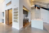 Located at 385 N Angier Ave NE in Atlanta's vibrant Old Fourth Ward neighborhood, this two-bedroom, two-bathroom loft spans two floors with a striking industrial-modern aesthetic. The main level impresses immediately with soaring double-height ceilings, polished concrete floors, and an expansive wall of steel-framed windows that flood the space with natural light and offer views of the surrounding streetscape. Exposed ductwork adds an authentic industrial character overhead, while a sleek kitchen features dark cabinetry, stainless steel appliances, and a marble-topped island with built-in sink. A striking black steel staircase with wood treads anchors the living area, ascending to the upper level beneath elegant pendant lighting. A barn door and built-in open shelving provide functional design accents on the main floor. A built-in bar area adds a refined entertaining touch. Upstairs, the second floor offers two well-proportioned bedrooms with plush carpeting, ceiling fans, and natural light from tall windows. The bathrooms are finished with light wood vanities, quartz countertops, large-format tile flooring, and LED-backlit mirrors. Closets feature custom dark wood built-in storage systems. The combination of raw industrial elements and polished modern finishes gives this loft a distinctive, sophisticated character.