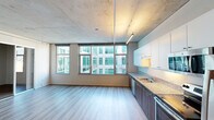 Located at 743 Tenth Ave in San Diego, CA, this single-floor urban residence offers a thoughtfully designed open-concept layout that blends modern finishes with industrial character. The exposed concrete ceiling is a defining architectural feature throughout the living area, lending the space a raw, loft-like aesthetic that is complemented by light wood-tone flooring underfoot.

The open living and kitchen area is bathed in natural light from a series of large windows that frame views of the surrounding urban courtyard. The kitchen is well-appointed with a full suite of stainless steel appliances — including a refrigerator, range, microwave, and dishwasher — paired with rich dark wood cabinetry, white upper cabinets, and granite-style countertops. A double-basin sink anchors the workspace.

A hallway connects the living area to the bedroom, which features sliding mirror-panel closet doors and additional windows that bring in natural light. The space also includes two bathrooms, each finished with warm wood vanity cabinetry, granite countertops, undermount sinks, and a tub-shower combination. Track lighting and recessed fixtures provide functional illumination throughout, rounding out this well-designed urban residence in the heart of San Diego.