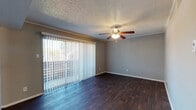 This single-floor residence offers a well-organized layout with a cohesive design throughout. The main living area is bright and open, featuring rich dark hardwood-style flooring, neutral gray walls, and a textured ceiling with crown molding. A ceiling fan with a built-in light fixture anchors the room, while a large sliding glass door dressed with vertical blinds allows generous natural light and provides views to an outdoor area. An adjacent dining or flex space connects seamlessly to the kitchen, maintaining the same flooring and open feel. The kitchen is a functional galley-style space outfitted with white cabinetry, dark granite countertops, a double stainless steel sink, and black appliances including a refrigerator and range. The bedrooms continue the neutral color palette, with one featuring plush carpet flooring and a ceiling fan, offering a softer, more restful atmosphere. The bathrooms are well-appointed with granite-topped vanities, white cabinetry, large mirrors, and bright overhead lighting. Textured ceilings and consistent trim details carry throughout the home, giving it a unified and polished appearance from room to room.