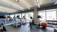 Located at 20 Hopmeadow in Aspen Glen, this fitness center is a well-appointed, single-floor exercise facility designed to support an active lifestyle. The space is outfitted with a selection of cardio equipment, including multiple treadmills and a stationary bike, complemented by additional fitness accessories such as an exercise ball. Durable, speckled rubber flooring covers the workout area, providing both safety and functionality for a variety of exercise routines. Large windows line the walls, flooding the room with natural light and offering pleasant views of the surrounding neighborhood, creating an open and inviting atmosphere. Mirrored walls further enhance the sense of space and allow users to monitor their form during workouts. Modern recessed and linear overhead lighting ensures the space remains bright and well-illuminated at all times. Decorative navy valances accent the windows, adding a polished, finished look to the room. The neutral color palette of warm beige walls and a white ceiling contributes to a clean, focused environment. Overall, this fitness center combines practical amenities with a comfortable, well-lit setting that encourages regular use.