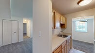 Located at 820 Carvel Dr in Dover, Delaware, this single-floor unit offers a functional and straightforward layout across several well-defined living areas. The galley-style kitchen is efficiently designed with warm honey-toned wood cabinetry lining both walls, providing ample upper and lower storage. It features light-toned countertops, a stainless steel sink, a white range, and a full-size refrigerator. Tile flooring runs throughout the kitchen, and a window at the end of the galley allows natural light to filter in. The spacious living area is finished with neutral wall-to-wall carpeting and features multiple windows that bring in generous natural light, contributing to an open and airy feel. Ceiling vents indicate a central HVAC system throughout. The bedrooms are carpeted and neutrally finished, with one room featuring a double-door closet and a window, while additional rooms offer built-in shelving and flexible use potential. The bathroom includes a full tub-and-shower combination with classic white and blue tile surround, accented by a blue tile border, giving it a retro, clean aesthetic. Overall, the unit presents a practical and livable space in a residential Dover neighborhood.