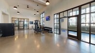 Located at 20 Romney St in Charleston, SC, this single-floor fitness center offers a comprehensive and thoughtfully designed workout facility. The main gym area is expansive, featuring polished concrete floors that lend a modern, industrial aesthetic throughout. Abundant natural light pours in through large, steel-framed multi-pane windows, creating a bright and energizing atmosphere. Pendant lights and ceiling fans are suspended overhead, contributing to both the aesthetic appeal and comfort of the space.

The main workout floor is equipped with a full rack of dumbbells, a cable and weight machine system, adjustable benches, and a dedicated section for cardio equipment including treadmills and an elliptical. Wall-mounted televisions are positioned throughout for entertainment during workouts. Large mirrors line sections of the walls, amplifying the sense of space and allowing users to monitor their form.

A separate studio room, accessed through steel-framed glass doors, provides a dedicated space for yoga, stretching, and mindfulness exercises. This room features yoga mats, stability balls, and a wall-mounted TV, with oversized windows offering views of the surrounding Charleston streetscape and greenery.

The facility's clean, neutral color palette and open layout create an inviting, professional environment well-suited for a wide range of fitness activities.