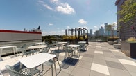 The Sky Deck is an elevated outdoor space designed to maximize its rooftop setting, offering sweeping panoramic views of the surrounding city skyline and tree canopy below. The open-air deck features a spacious tiled terrace finished in a clean grid pattern of light and medium grey pavers, providing a modern, polished aesthetic underfoot.

Throughout the deck, clusters of white bistro-style tables and latticed chairs are arranged to accommodate social gatherings while allowing unobstructed sightlines across the urban landscape. Striking black rectangular frame structures serve as architectural focal points and planters, adding vertical interest and greenery to the rooftop environment.

A full glass curtain wall with dark steel framing encloses an adjacent interior section, allowing natural light to flow through while maintaining visual connectivity between indoor and outdoor areas. This transparency reinforces the open, airy character of the space.

The property also features a ground-level pool area, accessible via a covered entry with rustic dark wood framing and stucco walls. The generously sized swimming pool is accompanied by a hot tub and broad sun deck lined with lounge chairs and patio umbrellas, creating a resort-like outdoor retreat. Together, the Sky Deck and pool area offer a well-rounded outdoor amenity experience suited for both relaxation and socializing.