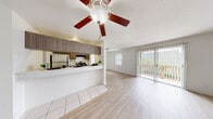 This single-floor unit offers a clean, functional layout designed for comfortable everyday living. The open-concept living and dining area is finished with light wood-look flooring and features a ceiling fan with light fixture overhead. Large sliding glass doors flood the space with natural light and provide direct access to a private balcony overlooking greenery, creating a pleasant indoor-outdoor connection. A side window further brightens the living area, keeping the atmosphere airy and welcoming.

The galley-style kitchen is positioned adjacent to the living space and is accessible via a pass-through counter, offering a semi-open feel. It features medium-toned wood cabinetry, light countertops, tile flooring, a stainless steel sink, and black appliances including a refrigerator and electric range with overhead microwave ventilation. The layout is efficient and well-organized, with ample upper and lower cabinet storage.

The bedroom is a generously sized, quiet retreat finished with plush carpeting, a ceiling fan, a window with vertical blinds, and a built-in closet. An additional room with light wood-look flooring and a closet provides flexible use as a second bedroom or office. The bathroom includes a full tub-shower combination with white tile surround and chrome fixtures, maintaining a clean, minimal aesthetic throughout.