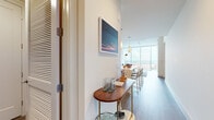 This single-floor residence offers a sophisticated, contemporary design highlighted by floor-to-ceiling windows that frame expansive city skyline views throughout the main living spaces. Light wood-tone flooring flows seamlessly across the open-concept layout, connecting the living area and kitchen.

The living room is bright and airy, anchored by oversized windows that flood the space with natural light and provide panoramic urban views. A welcoming entryway features a console table and louvered storage doors, offering a polished introduction to the home.

The kitchen is thoughtfully designed with a two-toned cabinetry scheme combining warm wood lower cabinets and matte upper cabinets. A generous island with a quartz countertop provides seating and additional workspace, complemented by a full suite of stainless steel appliances, a tile backsplash, and pendant lighting.

The bedroom continues the floor-to-ceiling window theme, offering striking cityscape views as a natural backdrop. The primary bathroom is elegantly appointed with large-format tile flooring, a wood-framed vanity mirror, a soaking tub, and a glass-enclosed shower with gray tile surround. A spacious walk-in closet with built-in shelving and hanging rods connects directly to the bathroom. A dedicated laundry area with a side-by-side washer and dryer completes this well-appointed residence.