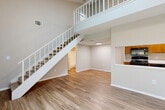 Located at 333 Lake in the Woods Drive in Melbourne, FL, this two-story, one-bedroom, two-bathroom home offers a thoughtfully designed layout spread across two floors. The main level features an open-concept living room, dining area, and kitchen, unified by light-toned hardwood-style flooring. Soaring ceilings with a dramatic staircase and an overlook from the upper loft create an airy, voluminous atmosphere throughout. A ceiling fan adds comfort to the living space. The kitchen is well-equipped with warm wood cabinetry, black appliances including a range, microwave, refrigerator, and dishwasher, plus white countertops and a pass-through window opening to the main living area. A sliding glass door leads from the main floor to a private balcony with lush outdoor views. The upper loft offers flexible use as an office, den, or additional living space. The spacious primary bedroom is carpeted and features corner windows that invite natural light and a ceiling fan overhead. Two closets provide ample storage, including a walk-in closet with wire shelving. Two full bathrooms feature tile flooring and wood vanities. A dedicated utility room completes the functional layout of this well-appointed home.