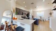 Located at 1601 E Highland Ave in Phoenix, Arizona, this three-bedroom, two-bathroom multi-story home is thoughtfully laid out across three floors. The ground level houses an attached garage with a concrete floor, ample wall space, and utility connections — providing practical storage and parking. A carpeted staircase with a sleek dark handrail connects the levels, featuring a built-in ledge and wall hooks at the entry landing.

The main living floor is the heart of the home, offering an open-concept kitchen and dining area bathed in natural light from large windows. The kitchen is outfitted with dark cabinetry, stainless steel appliances, a built-in microwave, and a generous white quartz island with bar seating. Light wood-style flooring flows seamlessly into the dining area, which features crown molding and a modern pendant light fixture. The adjacent living area is bright and airy with a wall-mounted TV setup and tall windows.

The upper floor hosts all three bedrooms and both bathrooms. The spacious primary bedroom includes vaulted ceilings, dual reach-in closets, plush carpeting, and a window seat. Secondary bedrooms are well-proportioned with neutral tones and carpet. The bathrooms feature dark wood vanities with white countertops and tub-shower combinations with wood-look tile flooring.