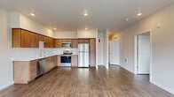 This single-floor unit is designed with a clean, modern aesthetic that emphasizes open living and functional design. The open-concept kitchen flows seamlessly into the main living area, creating a spacious, connected feel. The kitchen is outfitted with warm medium-toned wood cabinetry, a full suite of stainless steel appliances including a refrigerator, range, microwave, and dishwasher, and light countertops that complement the overall palette. Recessed lighting illuminates the space throughout.

The living area is generously sized and features wood-look flooring that runs consistently through the unit. A glass-paneled exterior door brings in natural light and provides outdoor access. Multiple bedrooms offer comfortable proportions, each featuring wood-look flooring, neutral walls, and windows with blinds that frame neighborhood views and allow ample natural light.

Two bathrooms serve the unit, each finished with wood-toned vanity cabinetry, white countertops, and wood-look flooring. One bathroom includes a walk-in shower, while the other features a tub-shower combination. A hallway connects the private areas of the unit, which also includes closet space with additional storage. The overall ambiance is bright, clean, and move-in ready.