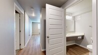 Located at 1525 W Havens Ave in Mitchell, South Dakota, this efficiently laid-out one-bedroom, one-bathroom unit offers a clean and modern living environment across a single floor. The kitchen serves as a standout feature, showcasing a large island with granite countertops, a stainless steel sink, and a full suite of stainless steel appliances including a refrigerator, range, and microwave. Warm-toned wood-look flooring runs throughout the kitchen and main living area, lending a cohesive and contemporary feel. A hallway with panel-style doors connects the living spaces to the private quarters, where the bedroom is finished with plush carpeting and includes double closets, providing ample storage. The neutral gray walls throughout the unit create a calm, versatile backdrop. The bathroom is thoughtfully appointed with wood-look flooring, a vanity featuring a large mirror and modern light fixture, and a full-size soaking tub and shower combination. Clean white fixtures and chrome hardware complete the space with a polished, functional aesthetic. Overall, the unit presents a practical and modern design suitable for comfortable everyday living.