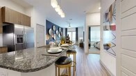 Located at 555 Promenade Pkwy in Irving, TX, this thoughtfully designed one-bedroom, one-bathroom residence offers a comfortable and modern living experience across a single floor. The open-concept layout seamlessly connects the kitchen, dining, and living areas, creating a cohesive and airy feel throughout.

The kitchen is a standout feature, showcasing rich wood cabinetry, dark granite countertops with an extended breakfast bar, stainless steel appliances, a tile backsplash, and wood-style flooring. Pendant lighting adds a refined touch overhead. The living room impresses with a bold navy accent wall adorned with decorative circular art pieces, large windows that invite natural light, and a ceiling fan for added comfort.

The bedroom is a serene retreat highlighted by a soft teal accent wall, plush carpeting, and generous natural light from large windows. It provides direct access to both the bathroom and a spacious walk-in closet, which features built-in shelving and multiple hanging rods for ample storage.

The bathroom is elegantly finished with warm wood vanity cabinetry, granite countertops, a deep soaking tub framed by marble-style tile surround, and wood-style flooring that ties the space together. High ceilings throughout enhance the overall sense of openness and volume.