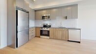 Located at 1110 Lawson Avenue in Kelowna, BC, this well-designed one-bedroom, one-bathroom unit offers a thoughtful layout with modern finishes throughout. Light hardwood flooring flows seamlessly across the entire space, creating a warm and cohesive feel.

The contemporary kitchen is a standout feature, equipped with stainless steel appliances including a range, microwave, refrigerator, and dishwasher. Two-tone cabinetry pairs warm wood lower cabinets with sleek grey upper units, complemented by a white subway tile backsplash and dark countertops, delivering a clean, modern aesthetic.

A well-proportioned hallway connects the kitchen to the remaining rooms, with recessed lighting overhead and doors leading to the closet, utility room, and bathroom. The bathroom features a full soaker tub and shower combination with brushed nickel fixtures, a wood-toned vanity with a grey countertop and undermount sink, and crisp white walls that keep the space feeling bright.

The bedroom is a comfortable, light-filled retreat with a large window offering open views of the surrounding Kelowna neighbourhood and distant landscape. A wall-mounted heating and cooling unit ensures year-round comfort. The entrance provides a practical welcome to the unit, rounding out this efficiently designed and move-in-ready space.