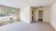 Located at 3400 Larchmont Ave in Alexandria, Virginia, Unit 1121 is a one-bedroom, one-bathroom residence designed for efficient, comfortable living. The layout includes a bedroom, kitchen, hallway, and bathroom, all contained on a single floor.

The living and bedroom area is generously sized relative to the overall footprint, featuring neutral wall-to-wall carpeting and cream-colored walls that create a bright, clean atmosphere. A baseboard heating unit provides warmth, and the open feel of the space allows for flexible furniture arrangements.

The kitchen is a functional galley-style space equipped with warm wood-toned cabinetry, a white gas range, and a stainless steel sink. A window above the kitchen area brings in natural light and offers a view of the surrounding greenery, making the space feel open and airy.

The bathroom showcases classic mid-century design, with pink wall tiles accented by bold black tile trim. A full soaking tub with an overhead shower, a pedestal-style sink, a framed mirror, and a frosted glass window complete the space, lending it a timeless, retro character.

A hallway connects the rooms and includes a closet, adding practical storage to the unit. Overall, Unit 1121 offers a straightforward, well-organized layout in a residential Alexandria neighborhood.