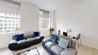 Located at 629 Euclid Ave in downtown Cleveland, OH, this one-bedroom, one-bathroom unit offers a well-designed, modern living environment with a thoughtful layout. Light wood-tone flooring flows throughout, complementing the bright, neutral color palette that gives the space an open and airy feel.

The combined kitchen and living area forms the heart of the unit. The kitchen is outfitted with high-gloss white cabinetry extending to the ceiling, stainless steel appliances including a range, microwave, and refrigerator, and a mosaic tile backsplash that adds a contemporary accent. A sleek white countertop island with an integrated sink provides both prep space and a natural divider between the kitchen and living area. Recessed lighting illuminates the kitchen efficiently.

The living room benefits from multiple large windows fitted with roller shades, framing direct views of the surrounding downtown Cleveland skyline. The bright, open layout comfortably accommodates a full seating arrangement.

The bedroom is a well-proportioned retreat featuring light wood flooring, crisp white walls, and a large window that continues the city view theme while allowing generous natural light. A dedicated closet provides ample storage.

The bathroom features floor-to-ceiling white square mosaic tiling, a full soaking tub with shower, and clean chrome fixtures, creating a crisp, modern aesthetic throughout.