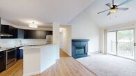 This two-bedroom, one-bathroom loft in Madison, WI offers a well-designed two-floor layout that maximizes both functionality and comfort. The main floor serves as the heart of the home, featuring an open-concept living area with plush carpeting, vaulted ceilings, and a ceiling fan overhead. A striking staircase with sleek black metal railings leads to the upper level, while sliding glass doors open to an outdoor balcony, flooding the space with natural light and providing access to outdoor views. A wall-mounted HVAC unit and baseboard heating ensure year-round comfort. The kitchen is thoughtfully appointed with dark cabinetry, stainless steel appliances, a peninsula with light countertops, and warm hardwood-style flooring that extends into the adjacent second bedroom — a versatile space with clean white walls and wood flooring. The upper-level primary bedroom is generously sized with soft carpeting, crisp white walls, and a closet with paneled doors. A hallway with a drum pendant light connects the bedroom to a full bathroom finished with dark tile. The overall aesthetic is clean and neutral throughout, creating a bright, move-in-ready living environment.