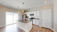 Located at 2507 Forest Villas in Chattanooga, TN, this single-story home presents a cohesive, well-appointed interior finished with consistent wood-look flooring and neutral warm-gray tones throughout. Crown molding accents the main living and kitchen areas, lending a polished, traditional character to the space.

The kitchen serves as a central highlight, showcasing a large island with dark granite countertops, an undermount sink, and pendant lighting overhead. White shaker-style cabinetry lines the perimeter, complemented by a classic subway tile backsplash and matching granite counters along the walls. Stainless steel appliances, including a refrigerator, range, and microwave, complete the functional layout. A sliding glass door beside the kitchen fills the area with natural light and provides outdoor access.

The living areas are spacious and open, featuring crown molding, ceiling fans with light fixtures, and large windows fitted with white blinds that allow for ample natural light. A dedicated hallway connects the rooms efficiently, with a utility closet housing the water heater. Additional rooms offer ceiling fans, wood-look flooring, and bright windows, providing flexible, comfortable spaces throughout this move-in-ready Chattanooga home.