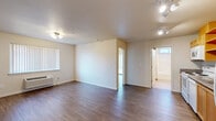 Located at 245 SE 146th Ave in Portland, Oregon, this single-floor, two-bedroom, one-bathroom unit offers a practical and efficiently designed layout. The open-concept living and kitchen area forms the heart of the unit, finished with durable wood-style flooring that extends consistently throughout the space. A wall-mounted HVAC unit and a large window with vertical blinds provide climate control and natural light to the living area.

The kitchen features light wood cabinetry, granite-style countertops, open shelving, and a full suite of white appliances including a range, dishwasher, microwave, and refrigerator. Track lighting overhead keeps the space well-lit and functional.

Both bedrooms are modestly sized with neutral walls and wood-style flooring. The primary bedroom includes a sliding-door closet with a built-in hanging rod, while the second bedroom offers ample wall outlets. Each room maintains a clean, minimalist character.

The bathroom is equipped with a shower-tub combination, a vanity with granite-style countertop, and a stacked washer and dryer unit, adding notable in-unit laundry convenience. A small window allows natural light into the bathroom, enhancing the bright, neutral aesthetic present throughout the entire unit.