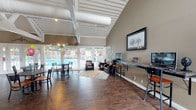 Located at 2102 E 51st St in Tulsa, Oklahoma, this single-story community clubhouse serves as a central hub for residents, combining functional amenities with an inviting atmosphere. The space is defined by its soaring vaulted ceilings with exposed white structural beams and cylindrical ductwork, lending an airy, open feel throughout.

Upon entry, a spacious reception and leasing area greets visitors with light tile flooring, a decorative chandelier, and an open floor plan that transitions seamlessly between zones. A prominent "Welcome Home" counter — finished with rich wood cabinetry and granite-style countertops — offers a self-serve coffee and refreshment station, setting a warm, community-oriented tone.

The lounge and gathering area features durable hardwood-style flooring and café-style seating with round bistro tables and bar-height chairs. Floor-to-ceiling glass doors and large windows flood this area with natural light and provide direct views and access to the outdoor pool area, making it ideal for community events and social gatherings.

A dedicated business center includes a long desk with computer workstations, offering residents a convenient space for remote work or study. The overall ambiance is warm and functional, with neutral earth-tone walls, tasteful artwork, and ample natural light throughout, creating a comfortable and practical communal environment.