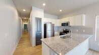 Located at 3850 Schafer Heights in Colorado Springs, Colorado, this single-floor home offers a clean, modern aesthetic throughout its well-designed layout. The open kitchen serves as a central highlight, showcasing granite countertops, a large peninsula with an undermount sink, crisp white cabinetry, a tile backsplash, and a full suite of stainless steel appliances including a refrigerator, electric range, and microwave. Natural light filters through slatted blinds, complementing the warm hardwood-style flooring that extends through the main living and kitchen areas. The bedrooms are carpeted for comfort and each features natural light from windows, a wall-mounted mini-split HVAC unit for individual climate control, and closet storage with distinctive dark-painted panel doors. The bathrooms are finished with matching granite vanities, wood-style flooring, and clean white fixtures — one offering a shower-tub combination and another with a dedicated walk-in shower stall. The home's neutral color palette, recessed lighting, and consistent design details create a cohesive and functional living environment suited for everyday comfort in the Colorado Springs area.