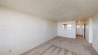 This single-floor unit features a straightforward layout connecting several distinct living spaces. The living area is generously proportioned, with neutral-toned carpet underfoot, textured walls, and a popcorn ceiling throughout. A pass-through opening connects the living area to the kitchen, allowing natural light to filter between spaces.

The kitchen is efficiently organized, offering warm wood-toned countertops, white cabinetry with ample storage above and below, and a full suite of white appliances including a refrigerator, gas range, and dishwasher. Light tile flooring completes the kitchen's clean, functional aesthetic.

The bedrooms are carpeted and feature textured walls consistent with the rest of the unit. One bedroom includes mirrored sliding closet doors, adding a sense of depth to the space. Wall-mounted HVAC units are present in the bedrooms, and windows provide natural light along with exterior views.

The bathroom includes a tiled tub-shower combination, a white vanity with a large mirrored medicine cabinet, and Hollywood-style vanity lighting overhead. Mosaic tile accents add a classic detail to the space.

Overall, the unit presents a neutral, functional interior with consistent finishes throughout, offering a practical and adaptable living environment.