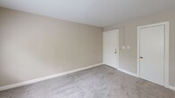 Located at 1301 N Queen St, Unit 201, in Arlington, VA, this one-bedroom, one-bathroom unit offers a practical and efficient single-floor layout. Neutral beige walls and soft gray carpeting are consistent throughout the living areas, creating a cohesive and understated aesthetic.

The living room provides a comfortable open area with carpeted flooring and a front entry door with gold-toned hardware. The space flows into a kitchen featuring wood-toned cabinetry, a white range, and a peninsula-style counter that separates the kitchen from the main living area, adding functional division without closing off the space.

The bedroom is a well-proportioned room finished with the same gray carpet and neutral walls. It features a large window that brings in natural light and offers a view of mature trees and the surrounding neighborhood. A double-door closet with gold hardware provides ample storage.

The bathroom includes a full soaking tub and shower combination with white subway tile surround and chrome fixtures. A frosted window above the tub allows for natural light while maintaining privacy.

Throughout the unit, clean white trim and baseboards provide a tidy, finished look. The overall ambiance is calm and neutral, offering a move-in-ready canvas in a convenient Arlington location.