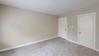 Located at 1301 N Queen St, Unit 201, in Arlington, VA, this one-bedroom, one-bathroom unit offers a practical and efficient single-floor layout. Neutral beige walls and soft gray carpeting are consistent throughout the living areas, creating a cohesive and understated aesthetic.

The living room provides a comfortable open area with carpeted flooring and a front entry door with gold-toned hardware. The space flows into a kitchen featuring wood-toned cabinetry, a white range, and a peninsula-style counter that separates the kitchen from the main living area, adding functional division without closing off the space.

The bedroom is a well-proportioned room finished with the same gray carpet and neutral walls. It features a large window that brings in natural light and offers a view of mature trees and the surrounding neighborhood. A double-door closet with gold hardware provides ample storage.

The bathroom includes a full soaking tub and shower combination with white subway tile surround and chrome fixtures. A frosted window above the tub allows for natural light while maintaining privacy.

Throughout the unit, clean white trim and baseboards provide a tidy, finished look. The overall ambiance is calm and neutral, offering a move-in-ready canvas in a convenient Arlington location.