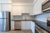 Located at 551 Vanier Dr in Kitchener, Ontario, this well-appointed 2-bedroom, 1-bathroom unit offers a clean, modern aesthetic throughout its thoughtfully designed single-floor layout. Light-toned hardwood flooring runs continuously across the living spaces, creating a bright and cohesive feel. The open-concept living and dining area is filled with natural light from large sliding glass doors that lead to a private balcony overlooking well-maintained green lawns and the surrounding community. The kitchen is efficiently designed with white cabinetry, a classic subway tile backsplash, dark countertops, and stainless steel appliances including a refrigerator, stove, and microwave — all complemented by a double sink. Two closets provide practical storage throughout the unit. Both bedrooms are comfortably sized, featuring large windows that invite natural light, baseboard heating, and neutral white walls, with the primary bedroom offering a generous footprint. The bathroom is finished with crisp white subway tile surrounding a full soaker tub and shower. Textured ceilings add character, while the clean white walls and light flooring throughout give the space a fresh, move-in-ready appearance.