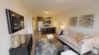 This contemporary single-floor residence offers a thoughtfully designed open-concept layout that seamlessly connects the living, dining, and kitchen areas. The living room is bright and welcoming, anchored by large floor-to-ceiling windows that flood the space with natural light and provide sweeping outdoor views. Wood-style flooring runs throughout, complementing the clean, modern aesthetic.

The kitchen is sleek and functional, featuring dark wood cabinetry that extends to the ceiling, a tiled backsplash in a soft aqua hue, stainless steel appliances including a gas range, microwave, and French door refrigerator, and a light quartz countertop. A peninsula with bar seating creates an ideal casual dining space and reinforces the open flow of the main living area.

The residence includes two bedrooms, each offering a calm and restful atmosphere with neutral walls, wood-style flooring, and ample closet storage. One bedroom features a built-in sliding closet with shelving. Both bathrooms are finished with large-format marble-style tile surrounds in the tub-shower combinations, grey floor tile, modern vanities with white countertops, and chrome fixtures, delivering a clean and polished look throughout.