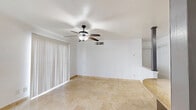 This single-floor unit offers a thoughtfully designed layout that maximizes its compact footprint. The open-plan living, dining, and kitchen area serves as the heart of the space, where travertine tile flooring flows seamlessly throughout, lending a warm, cohesive aesthetic. The living area is bright and airy, featuring a ceiling fan with a light fixture and a large sliding glass door dressed with vertical blinds that invites natural light while providing easy access to the outdoors.

The kitchen is a standout feature, outfitted with rich dark cabinetry, granite countertops, a mosaic tile backsplash, and stainless steel appliances including a range, microwave, and refrigerator. A peninsula with a granite surface and pendant lighting above adds both functionality and style, while decorative columns frame the transition between the kitchen and living areas.

The bathroom is well-appointed with a granite-topped dark wood vanity, a large framed mirror, and a full tub-shower combo, all finished with the same travertine tile that unifies the unit. Two closets and a hallway provide practical storage and circulation. The clean white walls throughout enhance the sense of openness, making this a functional and stylish living space.