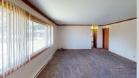 This single-story residence offers a straightforward, functional layout designed for comfortable everyday living. The floor plan, visible in the 3D overview, reveals a well-organized arrangement of rooms connected by accessible hallways, with distinct zones for living, cooking, sleeping, and bathing.

The living area is among the most notable spaces in the home, featuring plush carpeting, warm wood-trimmed windows that invite generous natural light, and a ceiling fan with an integrated window air conditioning unit. Baseboard heating runs along the exterior walls, and textured ceilings are found throughout much of the home. The large sliding windows offer views of surrounding greenery, creating a pleasant indoor-outdoor connection.

The galley-style kitchen is efficiently laid out, featuring warm oak cabinetry with ample upper and lower storage, light wood laminate flooring, a double sink, and white appliances including a full-size refrigerator. A flush-mount ceiling light provides functional illumination, and crown molding adds a finishing detail.

The bedrooms are carpeted and bright, each equipped with sliding windows framing outdoor views and baseboard heaters for year-round comfort. The bathroom includes a single-sink vanity with oak cabinetry, a full tub-shower combination, and a lighted mirror above the sink, all finished in clean, neutral tones.