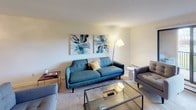 The Sycamore is a thoughtfully designed one-bedroom, one-bathroom residence that offers a comfortable and functional living environment across a single floor. The living room is a welcoming space featuring soft carpeting, a wall-mounted air conditioning unit, and a baseboard heating system, providing year-round comfort. Large sliding doors allow natural light to fill the room and offer views of the surrounding greenery. An adjacent dining area is defined by a stylish ceiling light fixture and decorative wall mirrors, creating a bright and intimate setting for meals. The kitchen is well-equipped with dark cabinetry, matching black appliances including a refrigerator, electric range, and dishwasher, complemented by ample counter space and hardwood-style flooring that adds warmth to the room. The bedroom is generously sized with plush carpeting, a large window framing pleasant outdoor views, and a sliding-door closet offering practical storage. The full bathroom features a dark vanity with a white countertop, a large mirror, and a shower-tub combination. Throughout the residence, neutral tones and consistent finishes create a cohesive and inviting atmosphere suited for comfortable everyday living.
