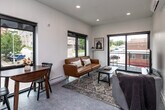 This well-designed single-floor unit offers a clean, contemporary aesthetic throughout its thoughtfully arranged layout. The open-concept living and kitchen area serves as the heart of the space, anchored by large black-framed windows that flood the interior with natural light and frame views of the surrounding urban streetscape. A sliding glass door opens directly onto a private balcony, extending the living space outdoors.

The kitchen is fully equipped with stainless steel appliances, including a gas range, refrigerator, and dishwasher. Two-tone cabinetry — warm natural wood lower cabinets paired with gray upper cabinets — is complemented by a dark subway tile backsplash and ample countertop space, creating a functional and stylish cooking environment.

The bedroom is a calm retreat, featuring a wall-mounted mini-split system, exposed beam ceiling details, and a large window that brings in generous natural light. The full bathroom is finished with large-format gray floor tiles, a warm wood vanity with a white countertop, and black hardware accents throughout.

A clean, bright hallway connects the rooms, equipped with recessed lighting and a digital thermostat. The consistent use of white walls, neutral flooring, and black-framed doors and windows creates a cohesive modern look throughout the entire space.