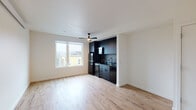 Located at 5620 N Interstate Ave in Portland, Oregon, this single-floor unit offers a thoughtfully designed living space with a clean, contemporary aesthetic. The open-concept main area combines the living room and kitchen, unified by light hardwood flooring that runs throughout and bright white walls that maximize the natural light streaming in from a large window with city views. A ceiling fan adds both function and style to the living area.

The kitchen is a standout feature, finished entirely in matte black cabinetry that extends from floor to ceiling, creating a bold contrast against the lighter surroundings. It is equipped with black appliances including a refrigerator, range, dishwasher, and built-in microwave, complemented by dark countertops and a sleek black sink with a modern faucet.

The bedroom is a calm, minimalist space with the same light hardwood flooring, recessed lighting, and a wall-mounted mini-split system for climate control. A sliding barn-style door adds a practical design touch.

The bathroom features a full tub-shower combination with a curved curtain rod, matte black fixtures and hardware throughout, and durable dark vinyl plank flooring, maintaining the unit's consistent modern design language. The space is clean-lined and move-in ready.