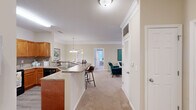 Located at Madison Park Drive in Huntsville, Alabama, this thoughtfully designed 2-bedroom, 2-bathroom residence offers a comfortable and functional single-story layout. The open-concept living area seamlessly connects the kitchen, dining, and living spaces, creating an inviting atmosphere ideal for both everyday living and entertaining. The kitchen features warm honey-toned cabinetry, granite-look countertops, black appliances including a refrigerator and range, a built-in wine rack, and a peninsula with bar seating. Crown molding and a pendant light fixture add a polished touch to the shared living and dining area, which is finished with plush carpeting throughout. The spacious primary bedroom includes a ceiling fan, ample closet space, and direct access to an en-suite bathroom. The second bedroom is generously sized, brightened by large windows that invite natural light, and is versatile enough to serve as a home office or guest room. Both bathrooms are finished with wood-toned vanity cabinetry and tub-shower combinations with tile accents. A dedicated laundry room with wire shelving provides practical storage. The overall aesthetic is warm and neutral, offering a comfortable and move-in-ready living environment.