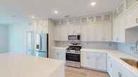 Located at 6755 W Arby Ave in Las Vegas, NV, this thoughtfully designed 2-bedroom, 3-bathroom unit offers a bright, modern living experience across a well-utilized single floor. The space features two fully equipped kitchens, each appointed with white shaker cabinetry extending to the ceiling with frosted glass upper panels, quartz countertops, light subway tile backsplashes, and stainless steel appliances including gas ranges, built-in microwaves, refrigerators, and dishwashers. Light wood-tone flooring flows consistently throughout, enhancing the clean, contemporary aesthetic. Both bedrooms are generously proportioned, featuring ceiling fans, sliding glass doors opening to private balconies with outdoor views, and en-suite bathrooms. The primary bathroom connects to a spacious walk-in closet with multi-tier wire shelving, while additional bathrooms also offer walk-in closet access. Crisp white walls and recessed lighting create a bright, airy ambiance throughout. The open sightlines from the kitchen into the living areas and toward the large sliding glass doors allow abundant natural light to fill the space, making this Las Vegas unit feel open and inviting.