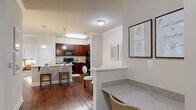 Located at Amelia Station in Clayton, NC, this single-story 2-bedroom, 2-bathroom residence offers a well-designed layout across a comfortable footprint. The open-concept living, dining, and kitchen area forms the heart of the home, highlighted by rich hardwood-style flooring, crown molding, and an abundance of natural light. The kitchen is appointed with deep-toned cabinetry, granite countertops, black appliances, pendant lighting, and a central island with bar seating — ideal for both cooking and casual dining. The adjacent dining area provides an intimate space for entertaining, while the living room opens to a private patio through glass French doors, bringing in additional natural light and outdoor access. The primary bedroom features plush carpeting, a ceiling fan, natural light from large windows, and a dedicated en-suite bathroom with granite vanity and rich wood cabinetry. The second bedroom also offers carpeting, a ceiling fan, and its own closet. A second full bathroom includes a tub/shower combo and matching vanity finishes. Five closets throughout the home — including walk-in options — provide generous storage. Additional spaces include a pantry, laundry room, utility room, hallway, and entrance foyer, rounding out this thoughtfully planned residence.