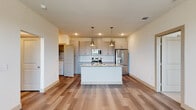 This well-appointed single-floor residence offers a thoughtfully designed layout that balances open communal spaces with comfortable private quarters. A welcoming hallway connects the various rooms, fitted with panel-style doors and wood-look flooring that flows throughout the main living areas.

The heart of the home is a generously sized open-concept kitchen, featuring soft gray shaker-style cabinetry extending to the ceiling for ample storage, a striking herringbone tile backsplash, and stone countertops with natural veining. A central island with a built-in sink provides additional workspace and casual seating. Stainless steel appliances, including a range, over-the-range microwave, and French door refrigerator, complete the kitchen. Pendant lighting above the island adds a warm, modern touch.

The primary bedroom is a spacious retreat with wood-look flooring, a ceiling fan, and large windows that invite natural light and outdoor views. It connects to a private en-suite bathroom featuring granite countertops, gray vanity cabinetry, and a glass-enclosed walk-in shower. An expansive walk-in closet with built-in shelving and hanging rods offers excellent storage.

A second bedroom is carpeted and bright, with dual windows overlooking the surrounding area. A second full bathroom with matching granite countertops and a bathtub serves this room. A dedicated laundry closet with a full-size washer and dryer adds everyday convenience.