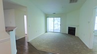 This single-floor residence at 4782 C offers a thoughtfully designed layout with a welcoming and airy atmosphere. The main living area is highlighted by soaring vaulted ceilings that amplify the sense of space, while light-toned walls create a bright and clean aesthetic throughout. A classic fireplace anchors one side of the room, providing a cozy focal point ideal for relaxing evenings. Flooring transitions seamlessly from warm hardwood near the entryway to plush wall-to-wall carpeting across the main living space, adding comfort underfoot. A large sliding glass door floods the interior with natural light and opens to a private balcony overlooking lush greenery, bringing a sense of the outdoors inside. Vertical blinds provide flexible light and privacy control. An adjacent hallway leads to additional rooms, suggesting a practical and functional floor plan. The unit's neutral color palette and clean architectural lines make it a versatile canvas ready for personalization. Overall, the space combines comfort, natural light, and classic design elements to create a livable and inviting environment.